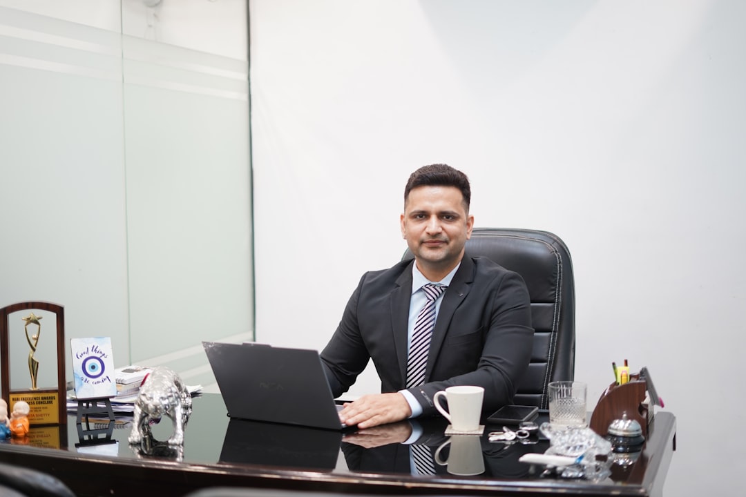 Man in suit sitting at desk with laptop and coffee.